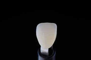 Close up shot ultra thin dental zirconium crown is held with tweezers with black background.