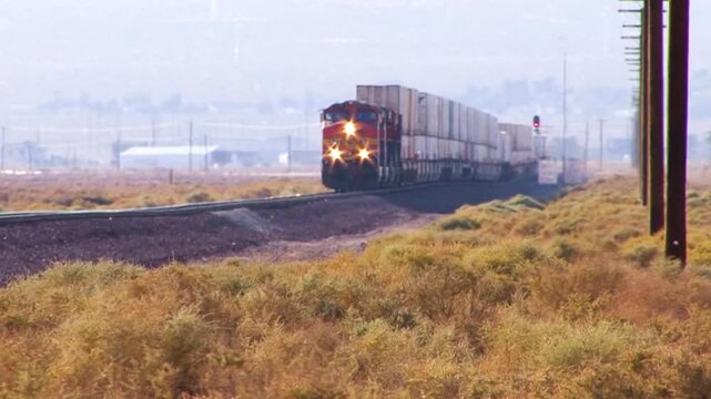 Long shot of an approaching double-stack container freight train crossing a windy, weedy  field.