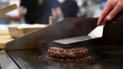 Expertly flipping a hamburger patty on a griddle. Perfect for food blogs, cooking tutorials, or restaurant promotions.