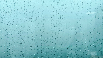 Raindrops on a glass window with a soft blue background, creating a moody and atmospheric texture.