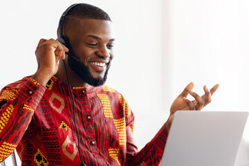 Positive Black Man In African Shirt Making Video Call With Laptop And Headset, Smiling Millennial...