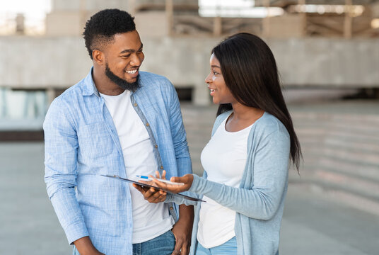 Black female volunteer conducting survey with young man on the street and writing down answers to clipboard, selective focus