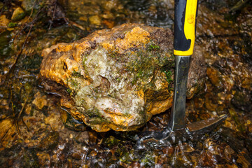 Rock splitting hammer stands next to a boulder from a stream, geological hike