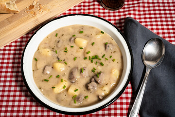 Creamy potato soup with chicken hearts garnished with chives in rustic enamel bowl