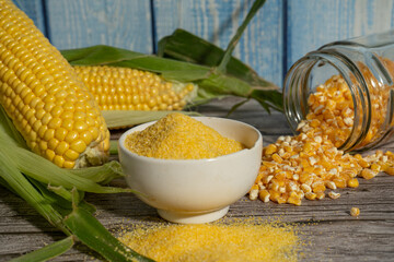Corn flour or polenta in a bowl with dried corn grains and fresh corn cobs on rustic wooden table