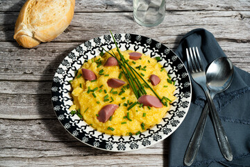 Creamy polenta with sausage and chives on rustic wooden table