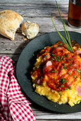 Creamy polenta topped with sausage ragu and fresh chives on rustic wooden table