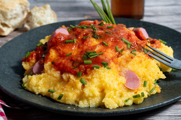 Creamy polenta with tomato sauce, sausage, and chives on black plate