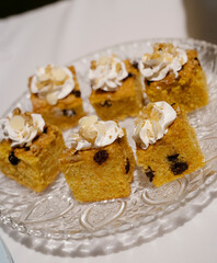 Sweet table snacks in a social event. Closeup view of carrot cake slices with a delicious frosting, served in a glass dish