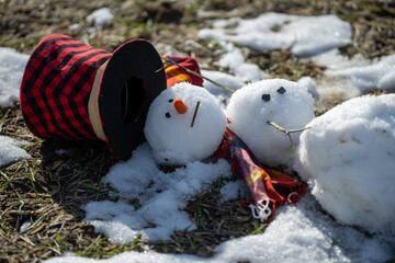 Snowman is melting outdoors in sunlight on snowy background mixed with green grass. Approaching...