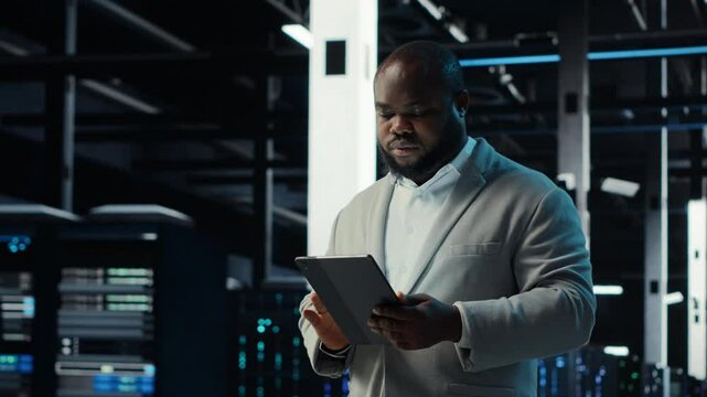 Server room admin doing troubleshooting to prevent downtime. IT specialist in data center reviewing reports and files, crosschecking network performance metrics and security logs, camera B