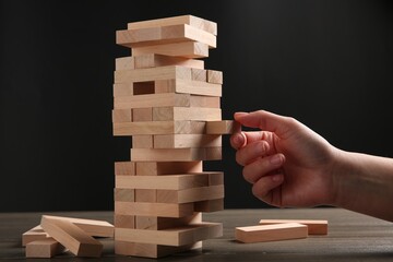 Lviv, Ukraine - December 04, 2023: Woman playing Jenga at table against dark gray background, closeup