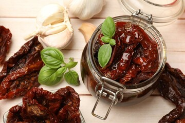 Tasty sun dried tomatoes and fresh vegetables on light wooden table, top view