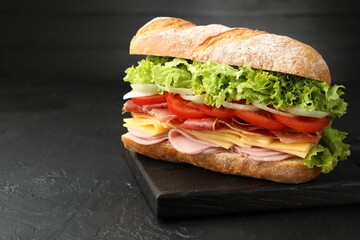 Tasty baguette sandwich with ham and vegetables on black table, closeup. Space for text