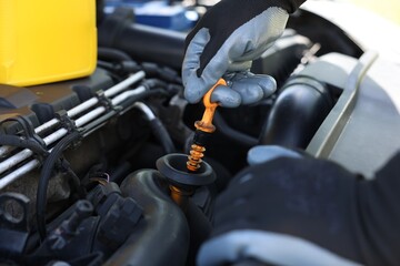 Worker checking motor oil level in car with dipstick, closeup