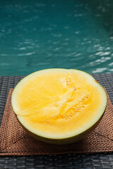 Half of ripe yellow watermelon on wicker table near swimming pool, closeup
