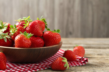 Fresh ripe strawberries in bowl on wooden table, closeup. Space for text
