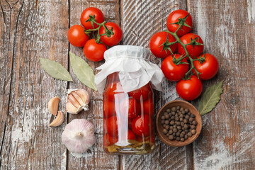 Tasty pickled tomatoes in jar and ingredients on wooden table, flat lay