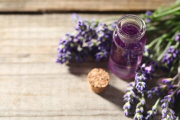 Natural essential oil and lavender flowers on wooden table, closeup. Space for text