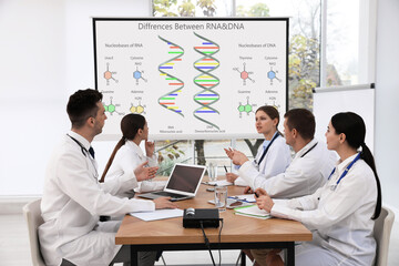 Team of doctors using video projector during conference about DNA and RNA indoors. Illustrations on...