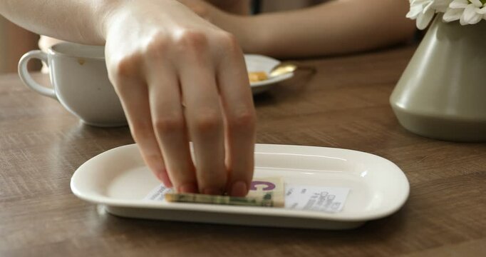 Woman putting tips onto plate at wooden table in cafe, selective focus