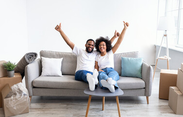 Family Housing. Joyful Black Spouses Celebrating Their Moving Day Sitting On Couch In New House,...