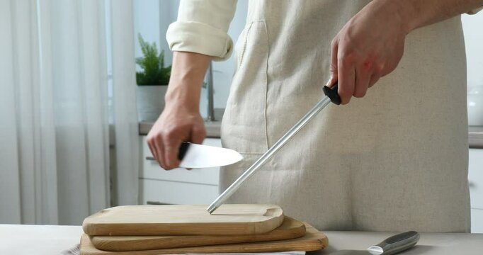 Man sharpening knife with sharpener at beige table indoors, closeup