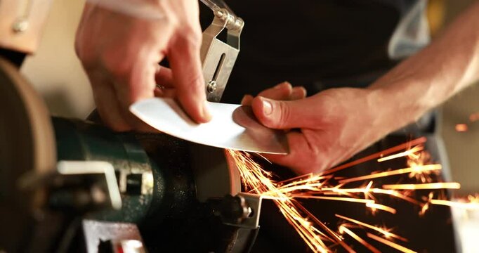 Man sharpening knife with bench grinder indoors, closeup