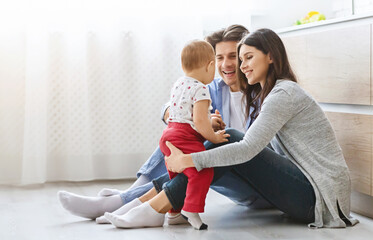 Family pastime. Cheerful mom and daddy playing with baby son on kitchen floor, free space