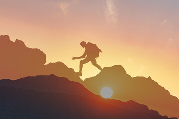 Man hiking on the edge of the mountain as a silhouette in colorful sunset, taking risk, vision,...