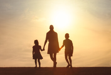 Obraz premium Mother little children holding hands walking in a grass field into the sunset. Motherhood, childhood, family, parenting concept 