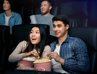 Happy young couple with popcorn watching movie in cinema