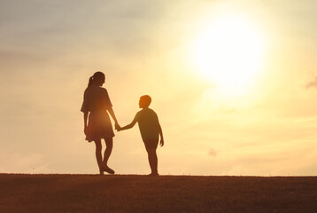 Fototapeta premium Mother, child holding hands walking in park in the morning sunshine, Family support, trust together, bonding in nature, Love, motherhood, parent help child concept
