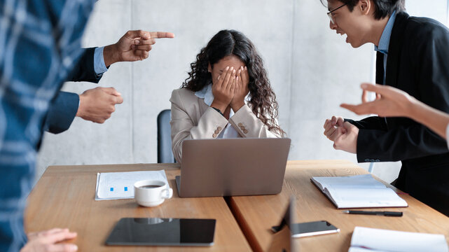 Workplace Conflict And Bullying. Aggressive Coworkers Yelling At Victimized Businesswoman Sitting At Desk In Modern Office. Corporate Communication Problem, Quarrels And Bad Attitude At Work