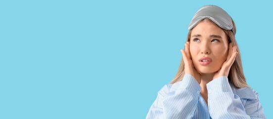 Young woman in pajamas suffering from loud noise on blue background with space for text