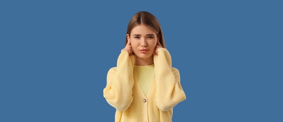 Young woman suffering from loud noise on blue background