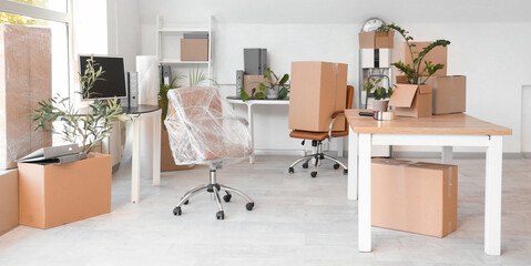 Obraz premium Desks with chairs and cardboard boxes in office on moving day