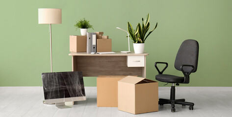 Workplace with cardboard boxes and chair near green wall in office on moving day