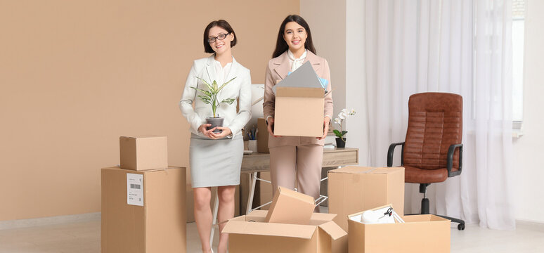 Young businesswomen packing things in office on moving day
