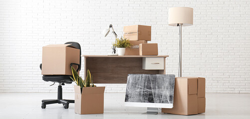 Desk with boxes, wrapped computer monitor and chair in office on moving day