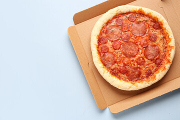 Cardboard box with delicious pepperoni pizza on blue background