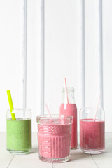 Glasses and bottles of colorful smoothie on white table