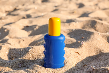Bottle of sunscreen cream on sand at sea beach