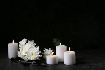 Burning candles, chrysanthemum flowers and black funeral ribbon on dark background