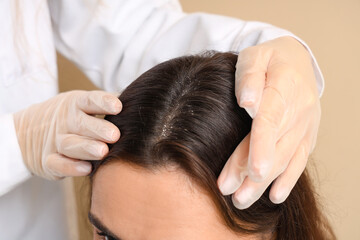 Trichologist examining young woman's scalp with dandruff on beige background, closeup