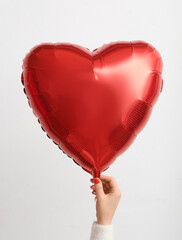 Female hand with red manicure holding heart shaped balloon on white background. Valentine's Day...