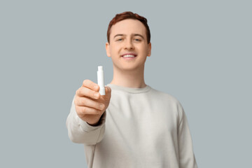 Handsome young man with lip balm on grey background