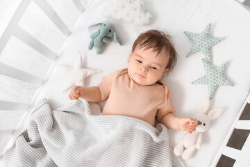 Cute little baby with plaid and toys lying in crib, top view