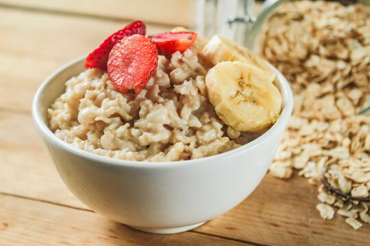 a bowl of oatmeal with strawberries and bananas on top, on a wooden table