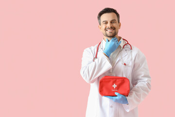 Male endocrinologist with first aid kit self-examining thyroid gland on pink background
